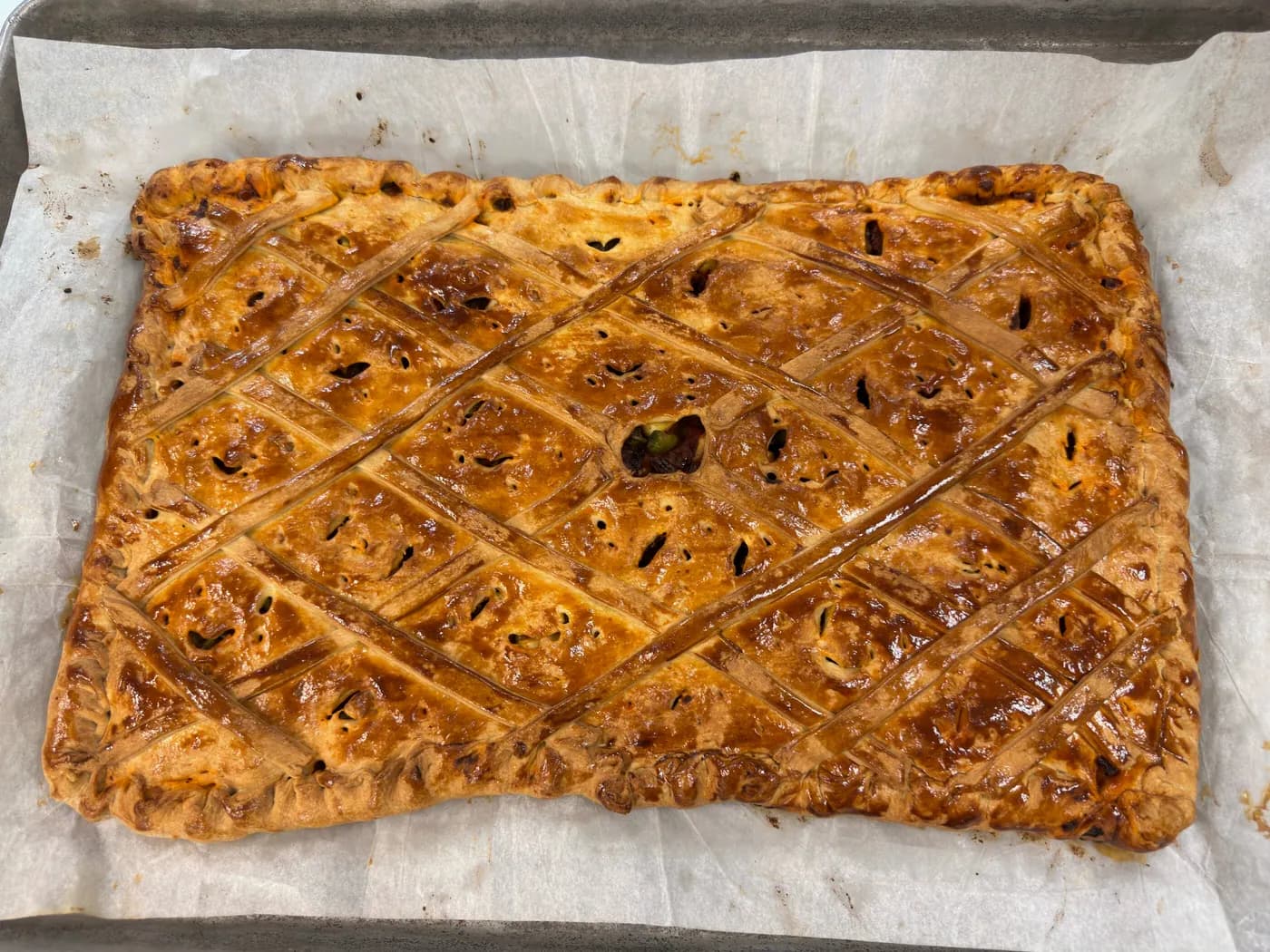 A whole lattice-topped empanada on baking paper