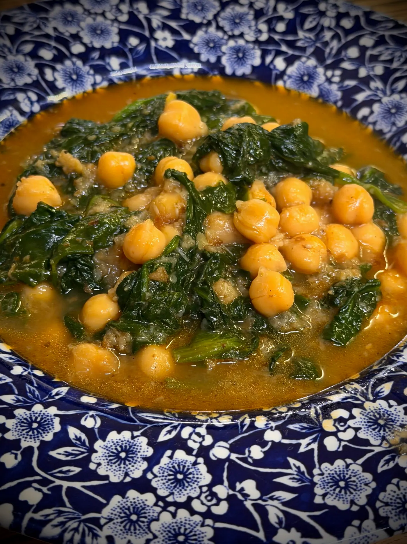 Spinach and chickpeas in a saffron broth in a blue-and-white bowl