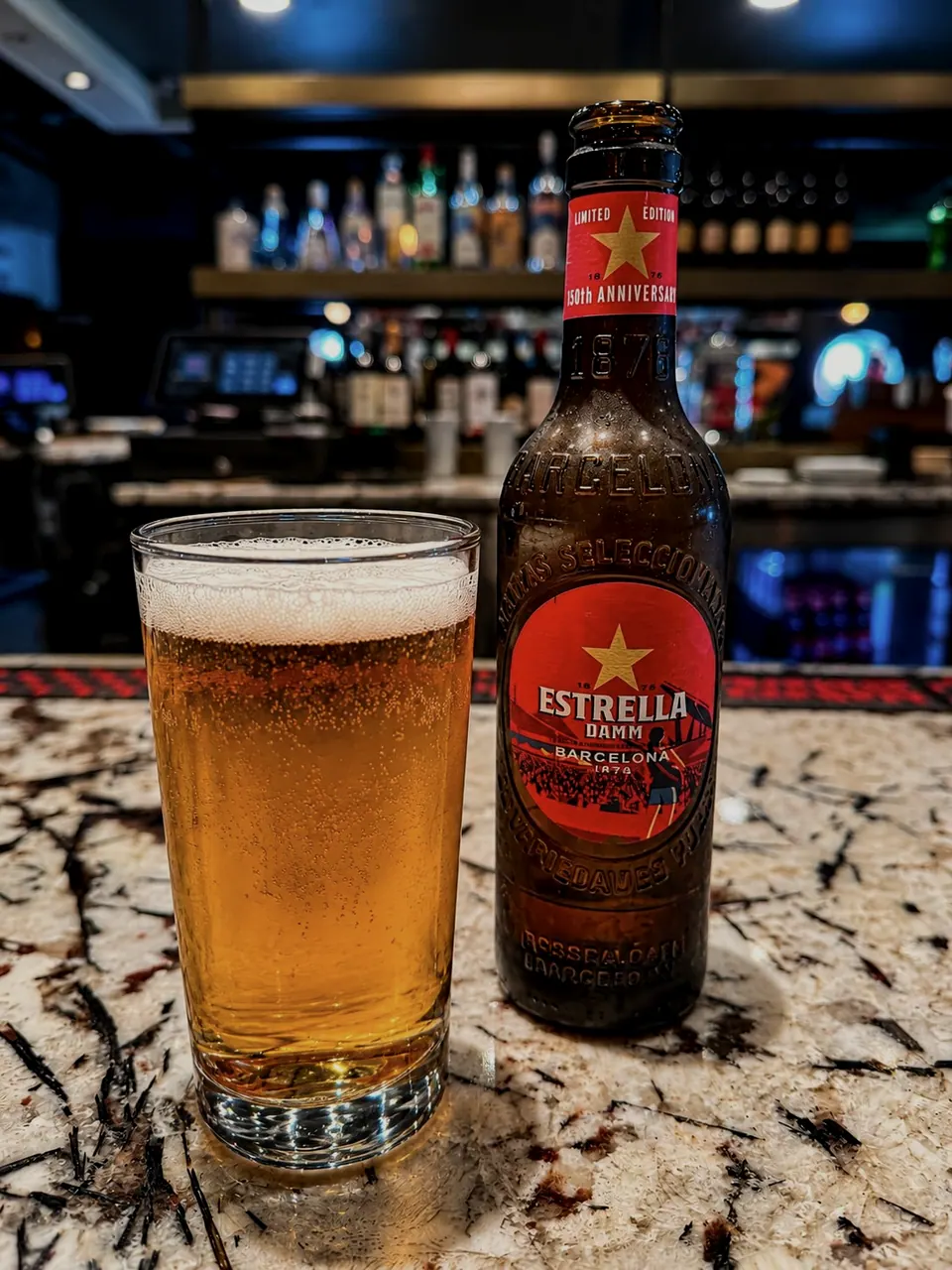 A glass of beer beside a bottle of Estrella Damm on the granite bar
