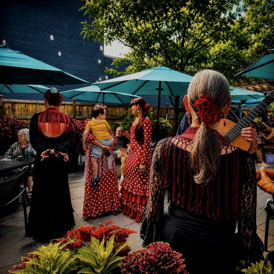 Flamenco dancers in ruffled dresses performing on a patio under umbrellas