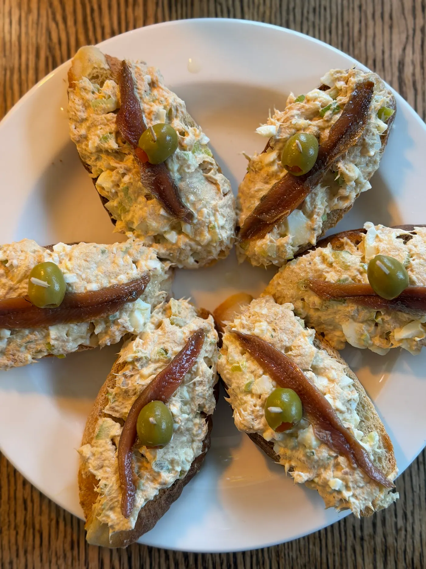 Toasts topped with a creamy spread, anchovies and olives, arranged on a plate