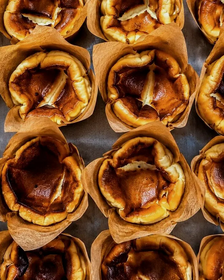 Mini burnt Basque cheesecakes in parchment on a sheet tray