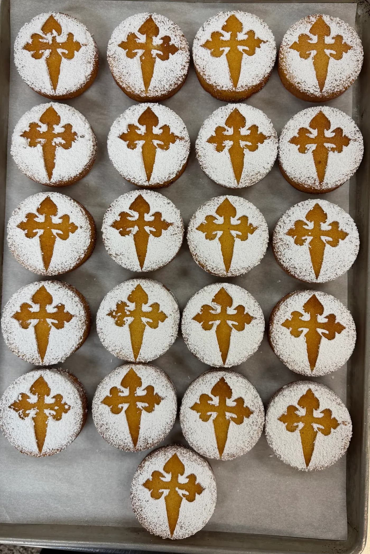 A tray of small almond cakes, each stenciled with the Cross of Saint James in powdered sugar