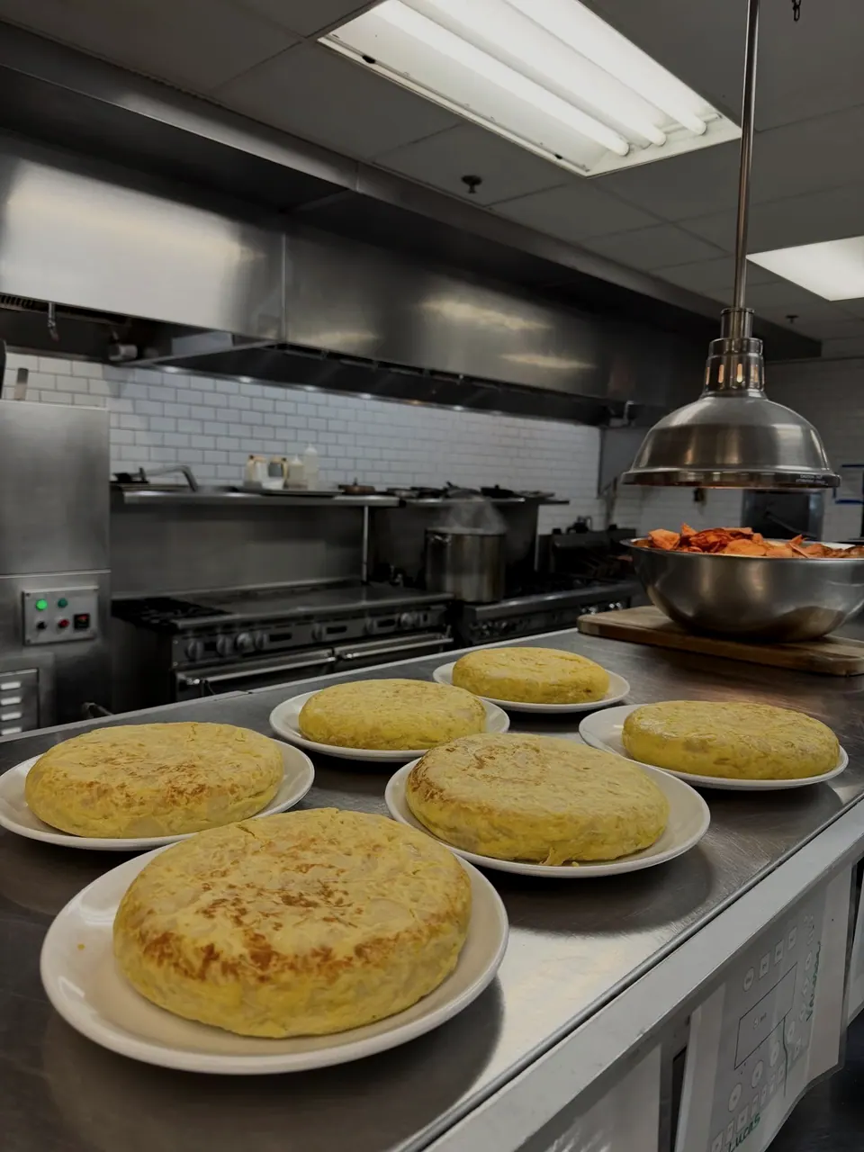 Round potato tortillas on plates along a stainless kitchen pass